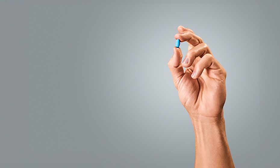 A hand holding up a blue pill