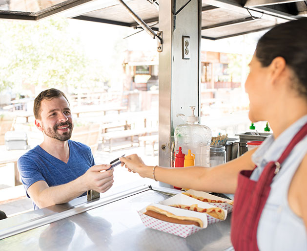A woman at a food stand handing a customer back his credit card 