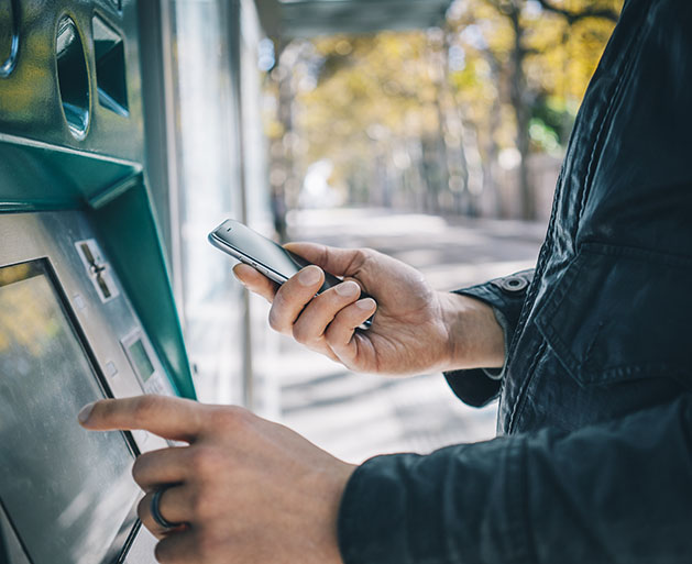 A man looking at his phone while at an ATM