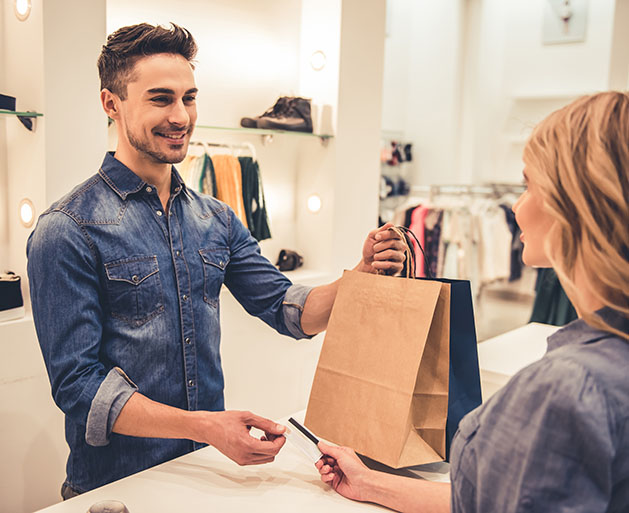 A male store clerk takes a customer's credit card while handing them their shopping bags